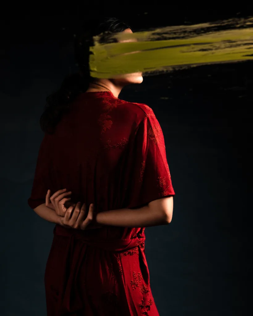 Una donna in abito rosso di spalle, con il volto coperto da una pennellata
